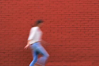blurred image of a woman running freely on the street by a brick wall