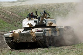 A Challenger 2 speeds down a green grassy hill in an exercise. The Challenger has sloped frontal armour on a massive boxy turret.