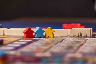 Red, blue, and yellow meeple figures in the game Merv