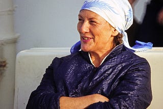 a woman with a blue jacket and light blue headscarf, smiling and looking confidently