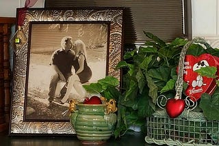 Framed photograph of a couple sitting on a garden bench and kissing, on a counter decorated for Valentine’s Day.