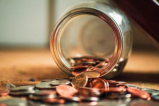 Photo of a glass jar spilling out coins.