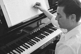 Black and white looking down as man writes at piano