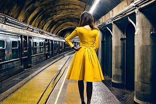 Girl in a bright yellow dress, standing in a dark underground subway.