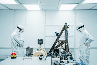 Scientists in a lab wearing full body suits examining equipment