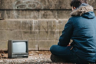 A man sitting on the ground in front of a small old tv
