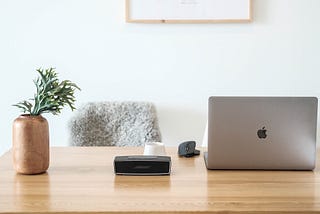 laptop on wooden desk next to plant and computer mouse. Gray fuzzy chair sits behind desk