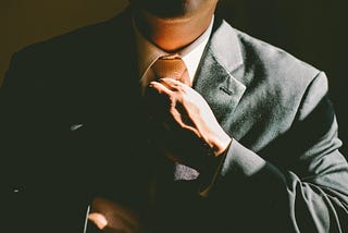 A man in a black suit loosening his tie