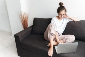 Image of smiling brunette woman typing on laptop while sitting on sofa