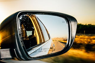 A side view mirror from a car, while the car is traveling on a road.