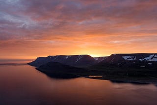 Sunrise coming up over sno capped mountains and reflecting on the water