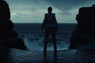 Rey stares out at the crashing waves on Ach-To, facing a grey and cloudy sky.