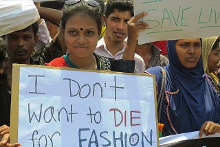 Woman standing in a protest holding a sign that says “I don’t want to die for fashion”