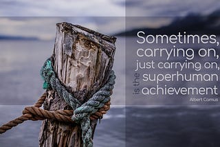 close up of a wooden pole in the water, with ropes around it, on a gloomy day. Text on the image is a quote by Albert Camus and it reads: Sometimes carrying on, just carrying on, is the superhuman achievement