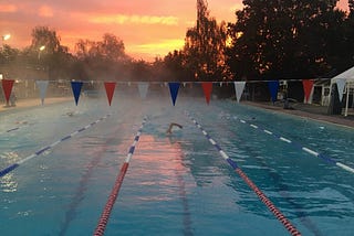 A swimmer swimming towards the camera in the middle of an outdoor pool at sunrise