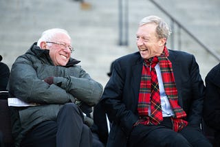 Bernie Sanders and Tom Steyer sit beside eachother laughing