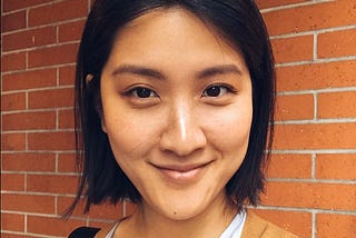 Headshot photo of a smiling Yehsong Kim wearing a light top with caramel-colored sweater