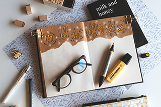 Desk blotter with planner book, writing utensils, paper clips, eyeglasses, and alphabet stamps