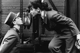 Black-and-white still from the film Closely Watched Trains where the actress Jitka Bendová leans down from a tain to kiss the actor Václav Neckář