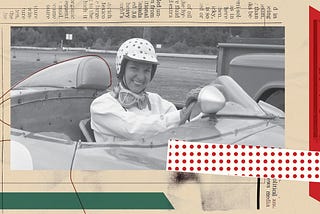 A black-and-white photo of a woman wearing a polka-dot helmet, with facing goggles around her neck, smiling from the driver’s seat of a racecar.