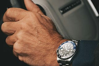 Close-up of a man’s hand wearing an expensive watch and suit.