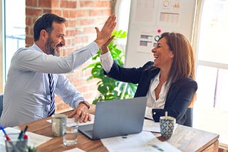 Colleagues congratulate each other while sitting at a shared office desk.