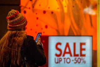 Consumer standing outside department store with a sale sign