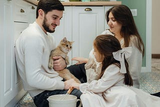 A family holding a cat and mixing dinner on the kitchen floor.