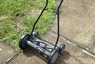 Hand powered rotary lawnmower sitting on a driveway.
