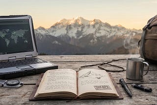 Alt-text: A rugged outdoor workspace set on a rustic wooden table with snow-capped mountains in the background. The gear laid out includes a heavy-duty laptop displaying a global network map, an open leather-bound journal with a mountain sketch and a “SHERPA INTELLIGENCE” stamp, a compass, keys on a carabiner, a tactical pen, a black USB drive, a steaming metal camp mug, a canvas backpack, and a pair of brown hiking boots.