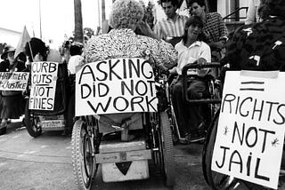Photo of wheelchair users protesting at the U.S. Capitol to push for passage of the Americans with Disabilities Act. One sign reads: “Asking did not work.” Link: https://www.wesa.fm/arts-sports-culture/2019-04-10/photo-exhibit-recalls-history-of-disability-rights-movement
