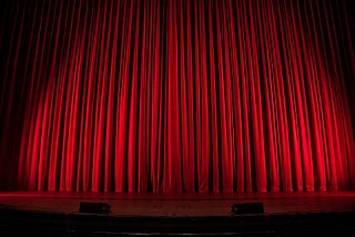 A closed red curtain on an empty theater stage