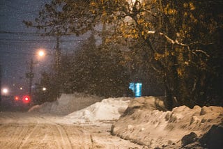 A dark and wintry city street with plowed snow piled on the curb.