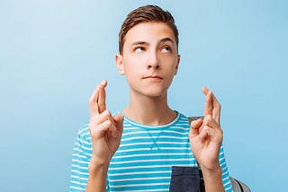 Teenage boy with fingers crossed, wishing for something.