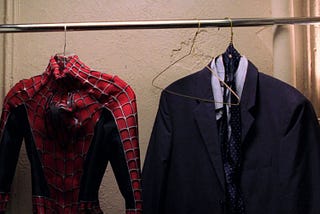 Imagem do filme Homem-Aranha 2. Em um cabideiro, estão duas roupas: um uniforme do super-herói, e um terno.