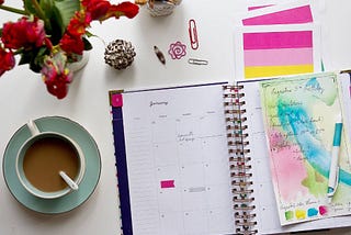 A notebook, some red flowers, and a cup of coffee.