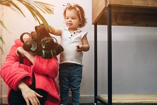 A mom sitting on the floor with curlers in her hair getting patted on the head by a child