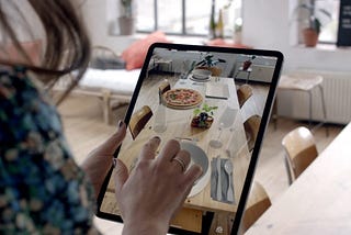 A picture of a woman who’s using an AR on iPad to place virtual food on the real table