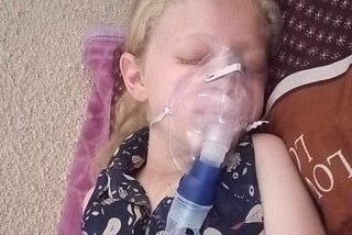 Picture of Judy (8 year old girl with fair skin and blonde hair) with an oxygen mask laying on blankets