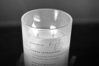 A lit candle with the words “moment to Reflect” written on it