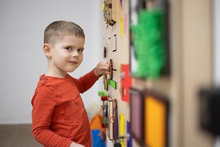 Young boy playing with a wall of sensory toys