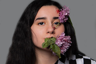A woman with a large flower in her mouth, and one covering her forehead