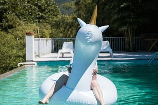 Woman sitting on an inflatable unicorn in a swimming pool