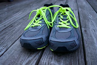 Pair of gray running shoes with neon green laces on a wooden deck.