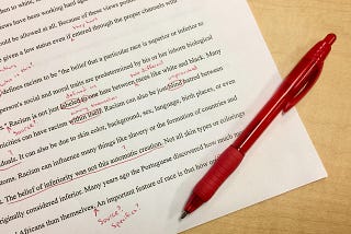 Photo of an essay on racism with red edits and a red ballpoint pen beside it, sitting on a light wooden surface