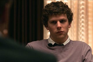 Jesse Eisenberg as Mark Zuckerberg in The Social Network, gazing grumpily.