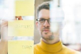 Portrait of the author Konrad Weber in front of a glass wall with sticky notes on it.