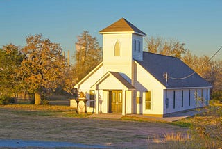 white church in a grassy clearing surrounded by trees