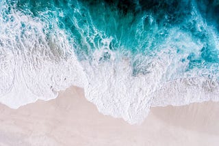 Aerial view of ocean waves hitting the sandy land.