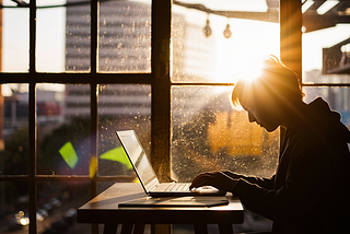 A freelancer working on a laptop by a window with natural light streaming in, emphasizing the role of natural light in maintaining circadian rhythms